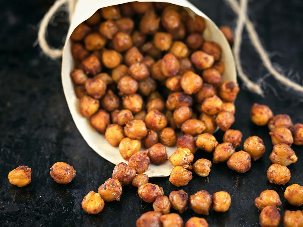 Golden roasted seasoned chickpeas spilling from a paper cone onto a dark surface.